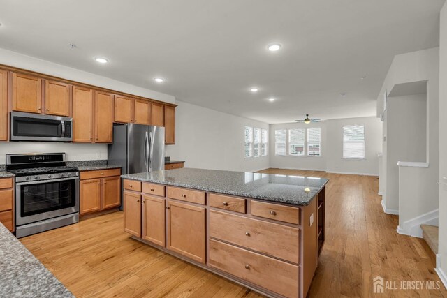 kitchen featuring ceiling fan, dark stone countertops, stainless steel appliances, a kitchen island, and light wood-type flooring