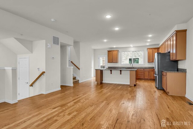 kitchen with sink, stainless steel fridge, a kitchen breakfast bar, light hardwood / wood-style floors, and a kitchen island