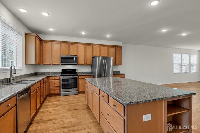 kitchen with sink, dark stone countertops, stainless steel appliances, a center island, and light wood-type flooring