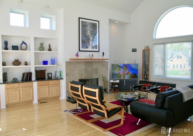 living area featuring light wood-style floors, a tiled fireplace, built in shelves, and a towering ceiling