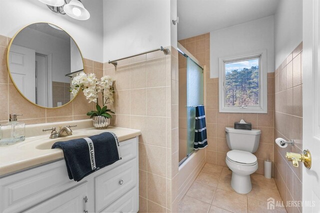bathroom with tile walls, tile patterned flooring, vanity, toilet, and enclosed tub / shower combo