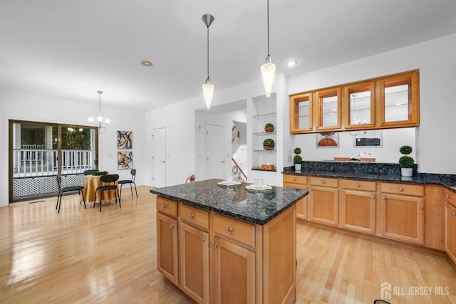 kitchen with decorative light fixtures, glass insert cabinets, a kitchen island, dark stone countertops, and light wood-type flooring