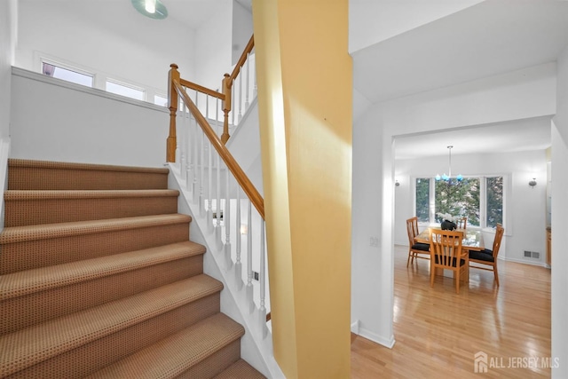 stairs featuring an inviting chandelier, visible vents, baseboards, and wood finished floors