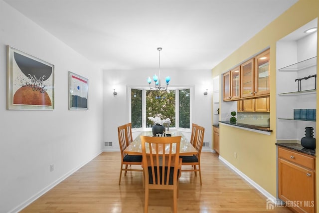 dining area with a chandelier, light wood-type flooring, visible vents, and baseboards