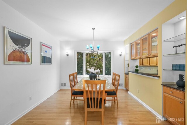 dining area with an inviting chandelier, light wood-style flooring, baseboards, and visible vents