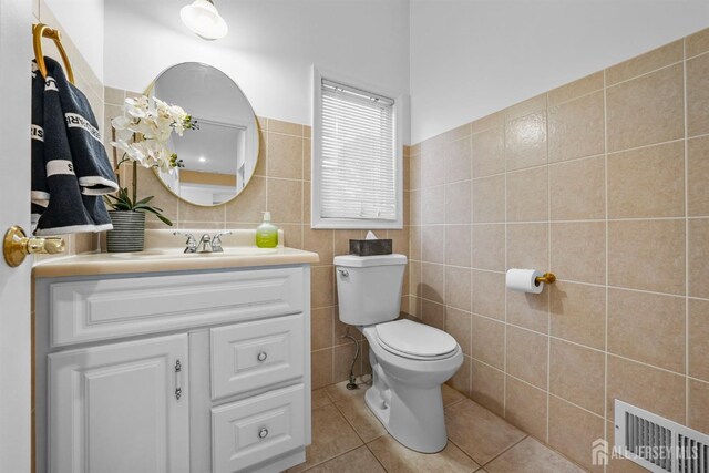 bathroom featuring vanity, toilet, tile patterned floors, tile walls, and visible vents