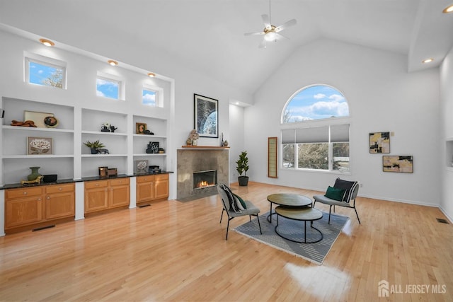 sitting room with light wood-type flooring, a fireplace with flush hearth, visible vents, and high vaulted ceiling