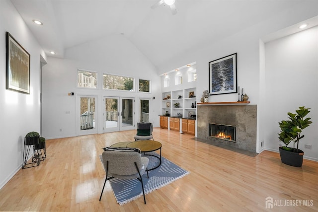 living room with a tile fireplace, french doors, light wood-style floors, built in shelves, and high vaulted ceiling