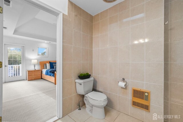 ensuite bathroom with toilet, tile patterned floors, heating unit, tile walls, and visible vents