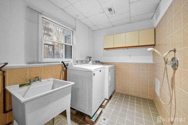 laundry room featuring independent washer and dryer, cabinet space, tile walls, light tile patterned floors, and visible vents