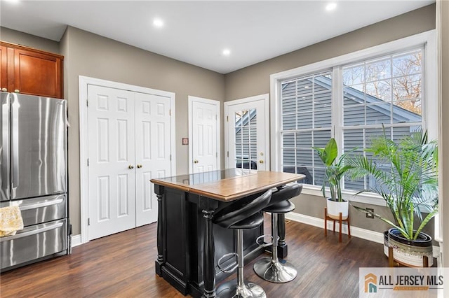 kitchen with freestanding refrigerator, brown cabinetry, recessed lighting, dark wood-style flooring, and baseboards