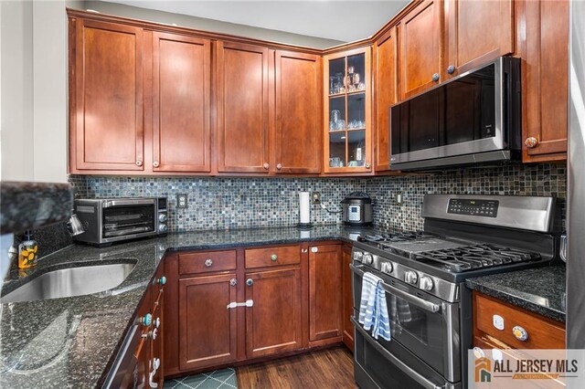 kitchen featuring glass insert cabinets, backsplash, dark wood-type flooring, dark stone counters, and appliances with stainless steel finishes