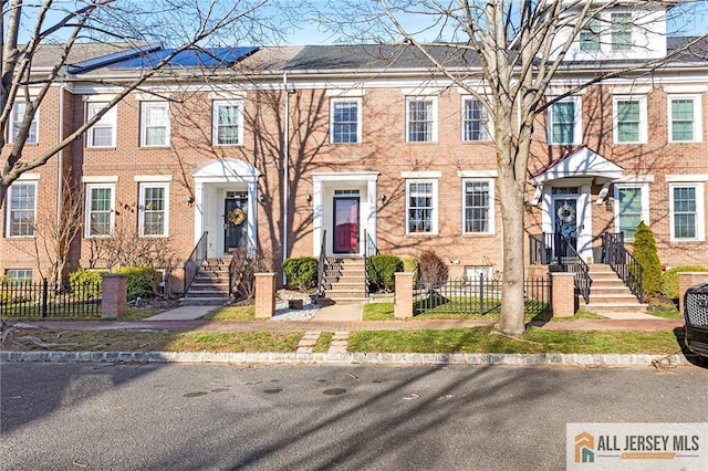 view of property with brick siding, entry steps, and fence