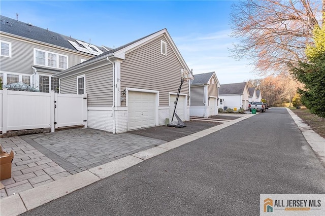 view of side of home featuring aphalt driveway, fence, a residential view, and a gate