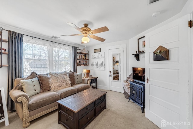 living room featuring a ceiling fan, visible vents, and light colored carpet