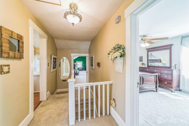 hallway with an upstairs landing, carpet, visible vents, and baseboards