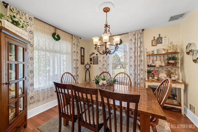 dining space featuring wood finished floors, visible vents, a chandelier, and baseboards