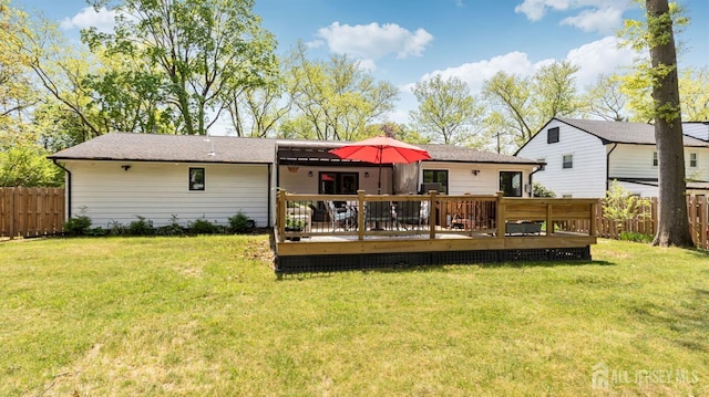 rear view of property featuring a yard, a wooden deck, and fence