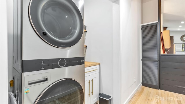 washroom with stacked washer and clothes dryer, wood finished floors, cabinet space, baseboards, and recessed lighting