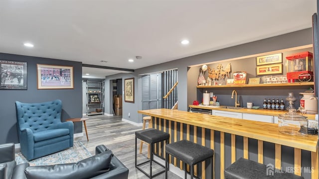 bar featuring wood finished floors, a sink, baseboards, wet bar, and recessed lighting