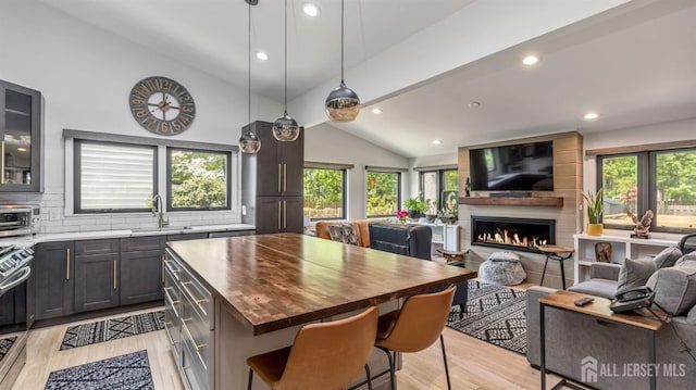 kitchen with a sink, butcher block countertops, lofted ceiling with beams, light wood-type flooring, and open floor plan