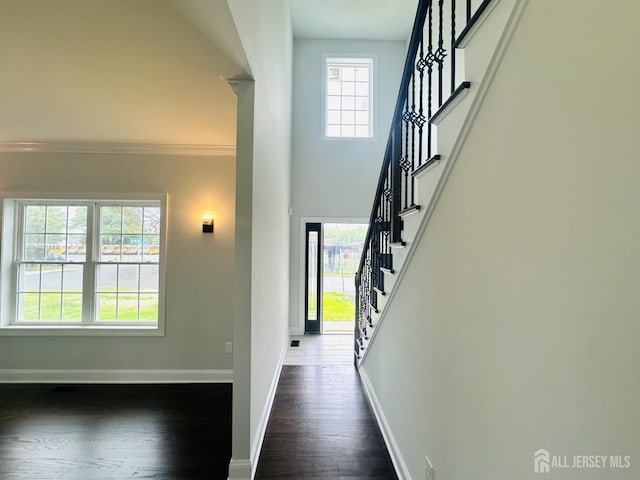 foyer entrance featuring plenty of natural light, dark wood-style floors, baseboards, stairs, and crown molding