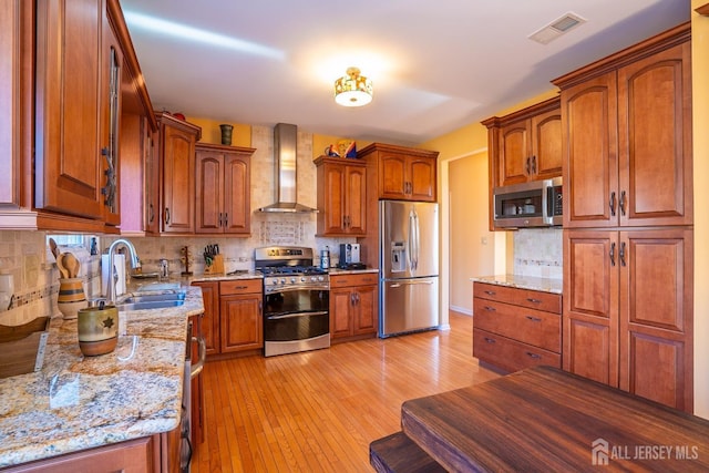 kitchen with light stone counters, appliances with stainless steel finishes, wall chimney exhaust hood, and sink