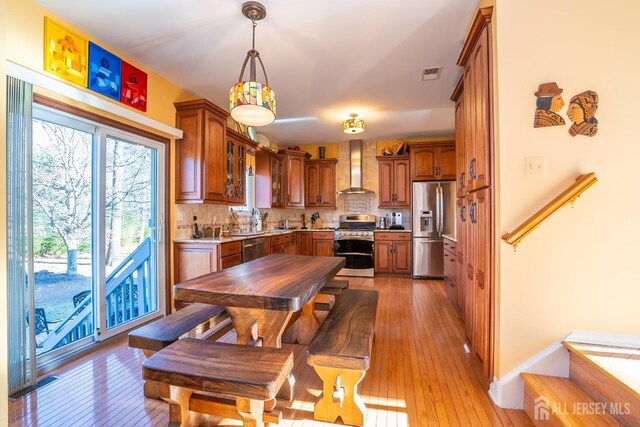 kitchen featuring light hardwood / wood-style flooring, hanging light fixtures, stainless steel appliances, tasteful backsplash, and wall chimney exhaust hood