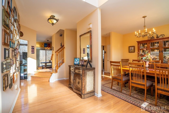 dining area with a chandelier, stairway, light wood-style flooring, and baseboards