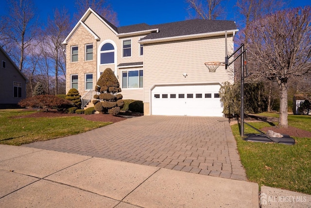 traditional-style home featuring decorative driveway, a front lawn, and an attached garage