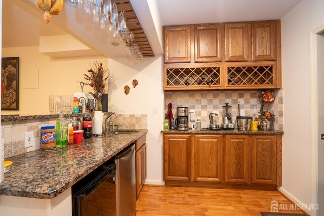 bar featuring dishwasher, sink, dark stone countertops, decorative backsplash, and light hardwood / wood-style flooring