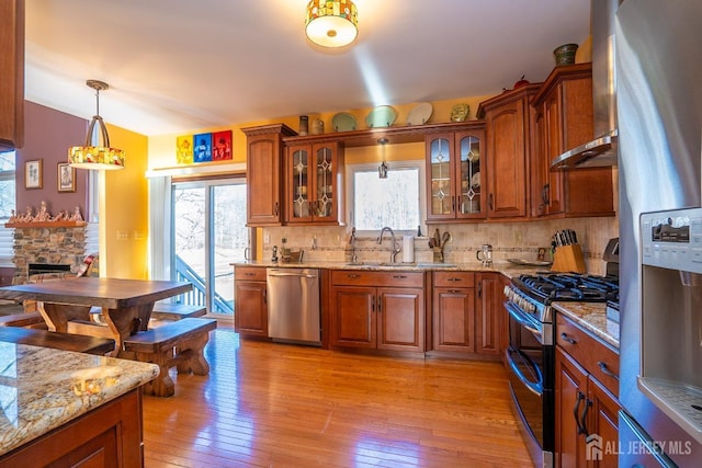 kitchen with appliances with stainless steel finishes, a stone fireplace, hanging light fixtures, light stone countertops, and wall chimney exhaust hood