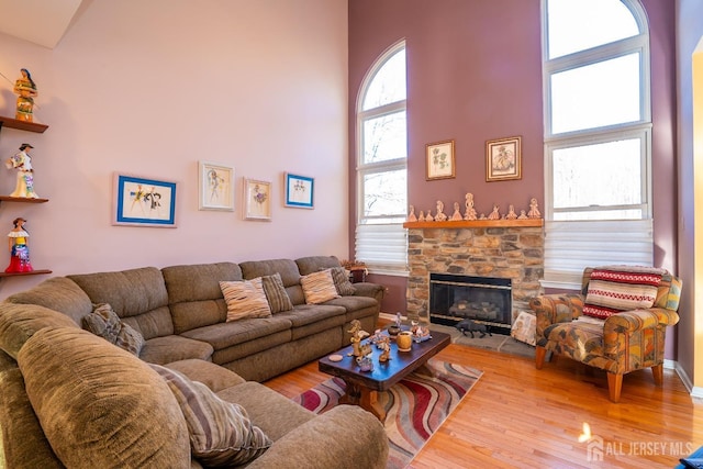 living room with hardwood / wood-style flooring, a stone fireplace, and a towering ceiling