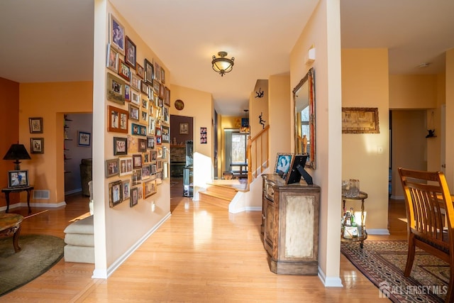 corridor featuring stairs, baseboards, visible vents, and light wood finished floors