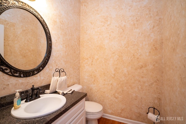 bathroom with toilet, vanity, baseboards, and wood finished floors