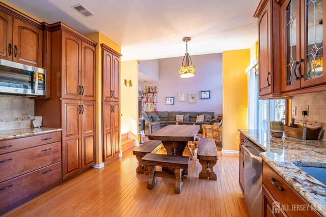 kitchen with light hardwood / wood-style flooring, appliances with stainless steel finishes, hanging light fixtures, tasteful backsplash, and light stone counters