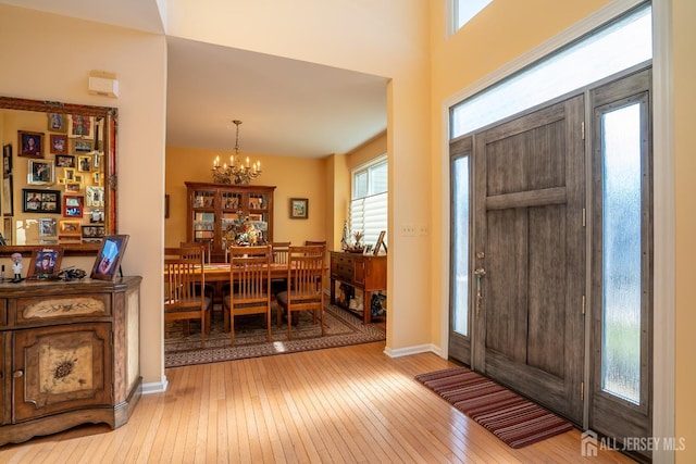 foyer entrance featuring a notable chandelier, a healthy amount of sunlight, baseboards, and light wood-style floors