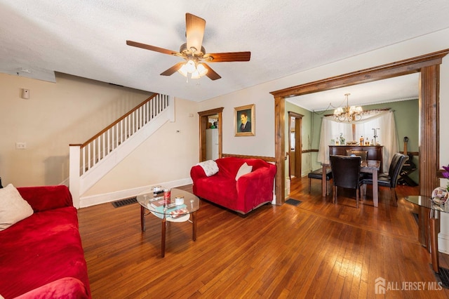 living room with dark wood-type flooring, ceiling fan with notable chandelier, and a textured ceiling