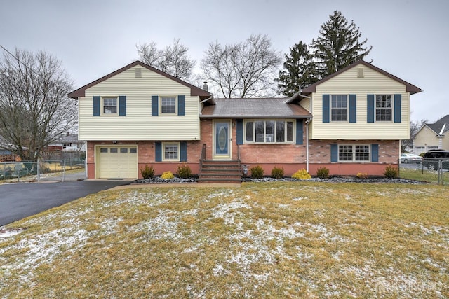 split level home with an attached garage, fence, aphalt driveway, and brick siding