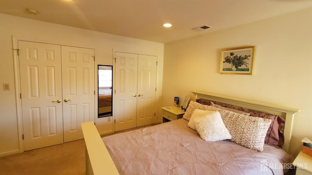 bedroom with recessed lighting, visible vents, light carpet, and two closets