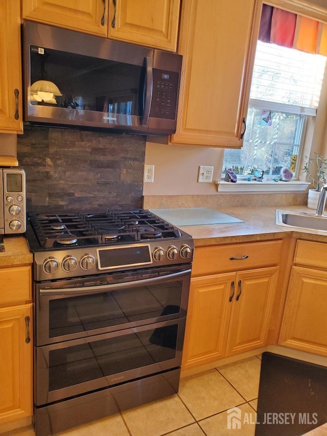 kitchen featuring light tile patterned floors, a sink, decorative backsplash, light countertops, and appliances with stainless steel finishes