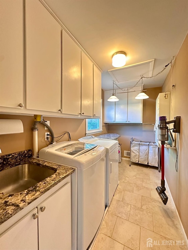 clothes washing area with independent washer and dryer, cabinet space, a sink, stone finish floor, and baseboards
