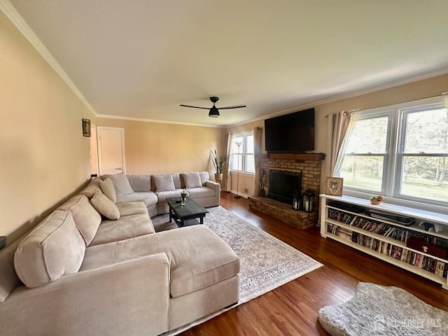 living area with crown molding, ceiling fan, a brick fireplace, and wood finished floors