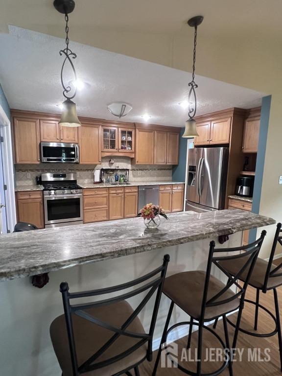 kitchen featuring hanging light fixtures, decorative backsplash, stainless steel appliances, and a kitchen bar