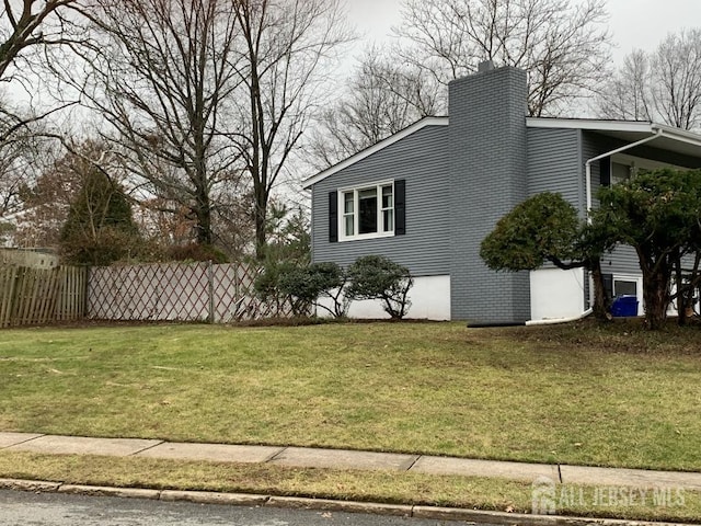 view of side of property featuring a lawn, fence, and a chimney