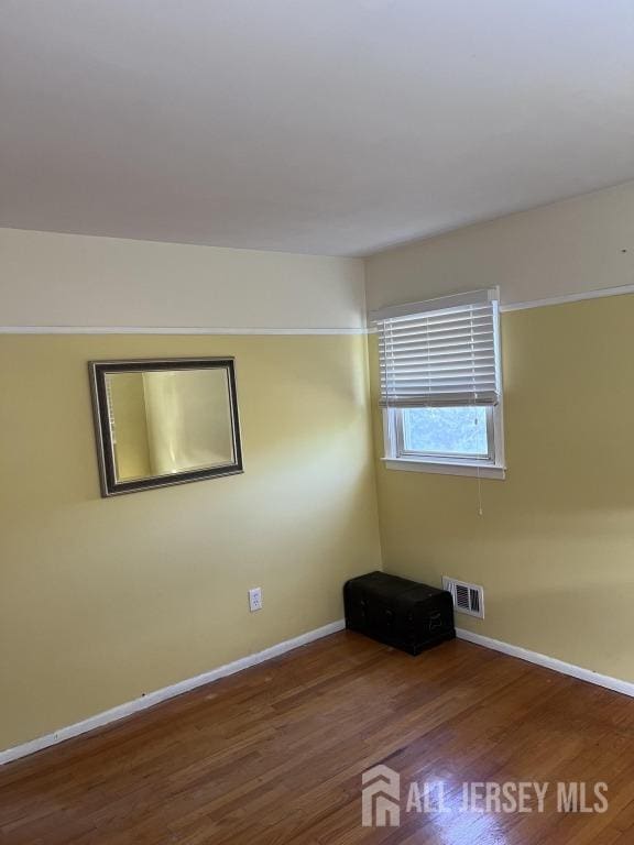 empty room featuring visible vents, baseboards, and wood finished floors