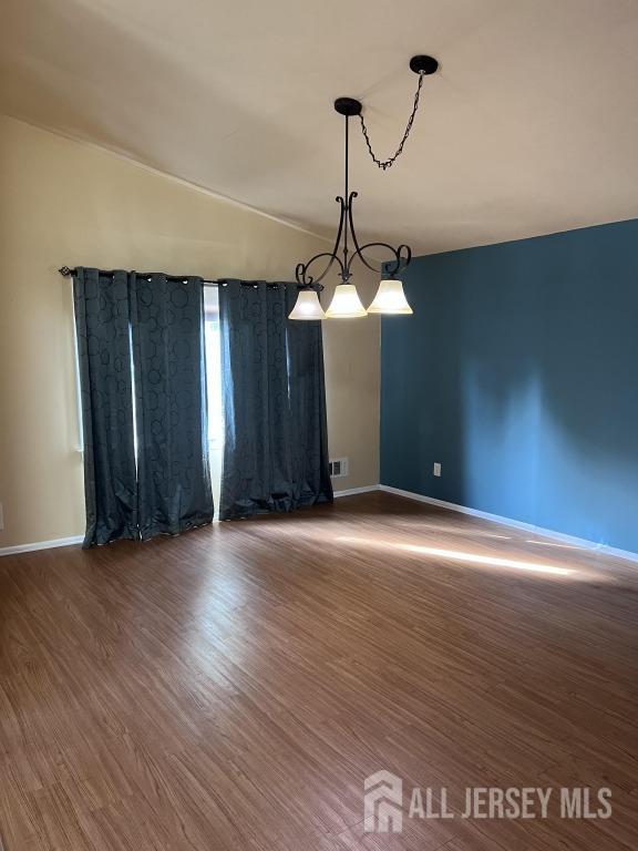 spare room with vaulted ceiling, wood finished floors, visible vents, and baseboards