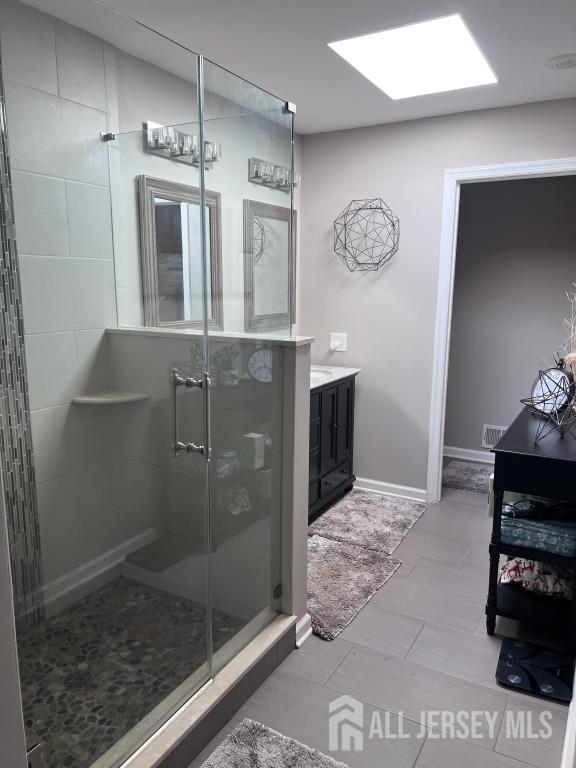 bathroom with visible vents, a skylight, a shower stall, baseboards, and vanity