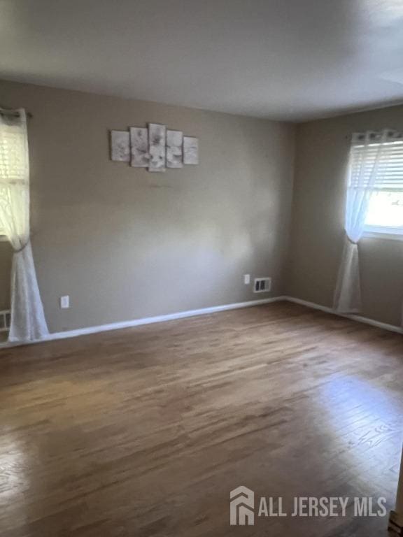 spare room featuring visible vents, baseboards, and wood finished floors