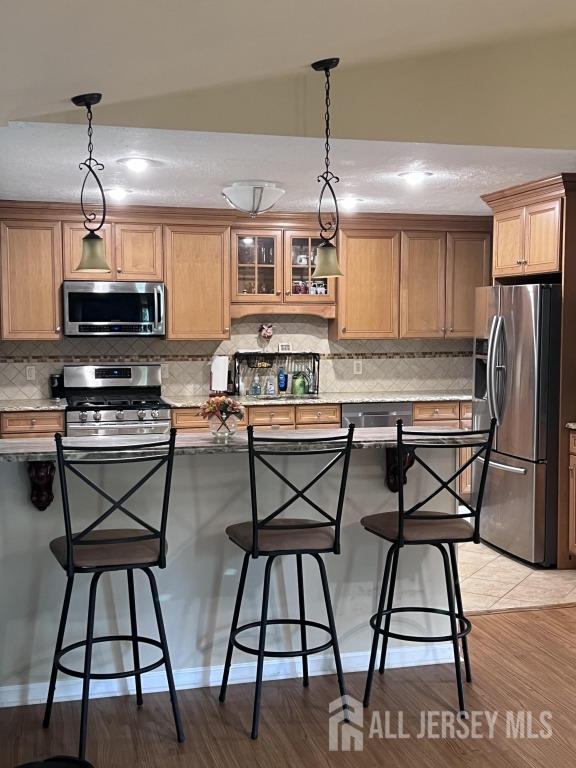 kitchen featuring decorative light fixtures, stainless steel appliances, backsplash, and a breakfast bar area